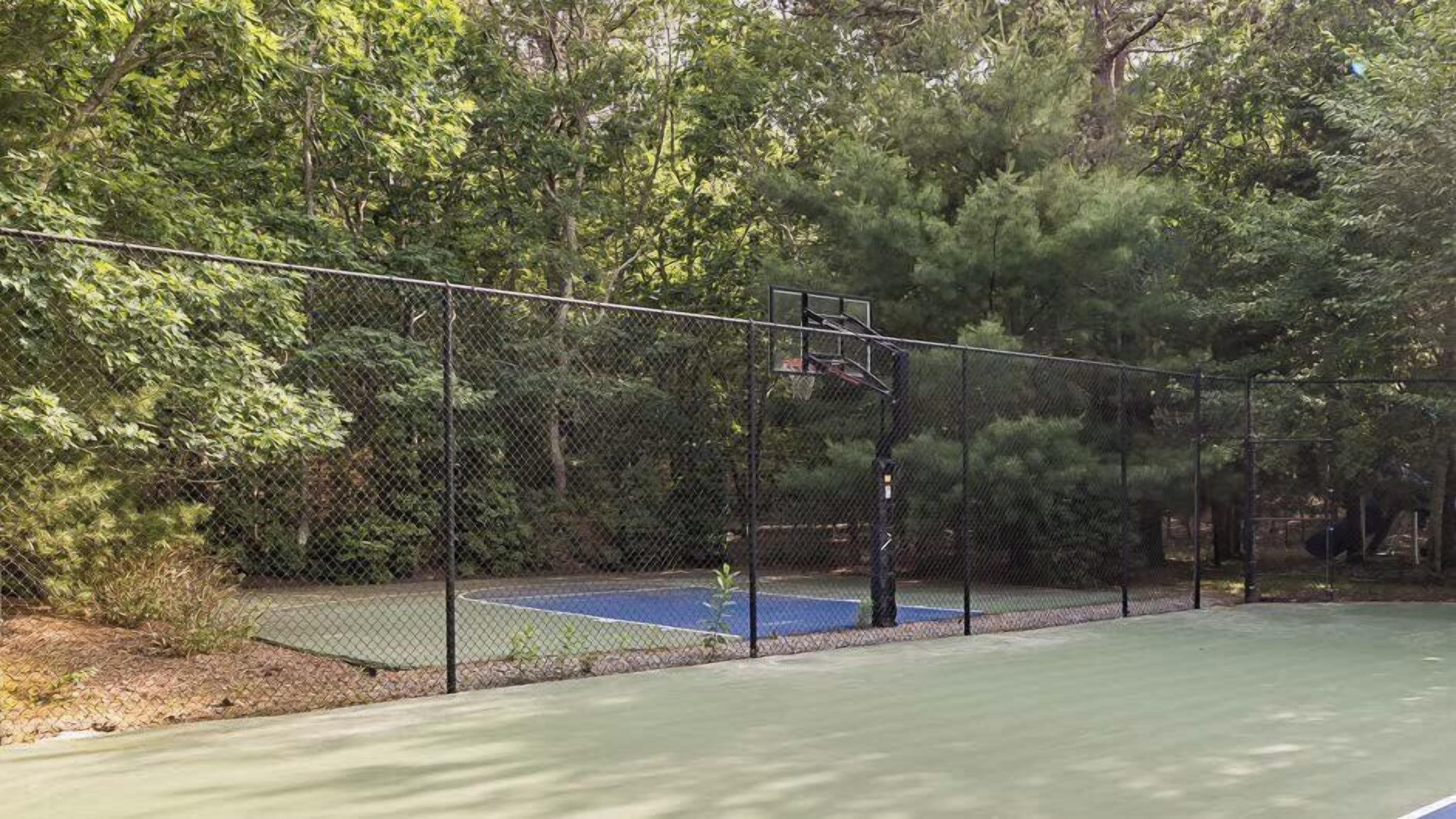 A tennis court enclosed by a chain-link fence, surrounded by trees.