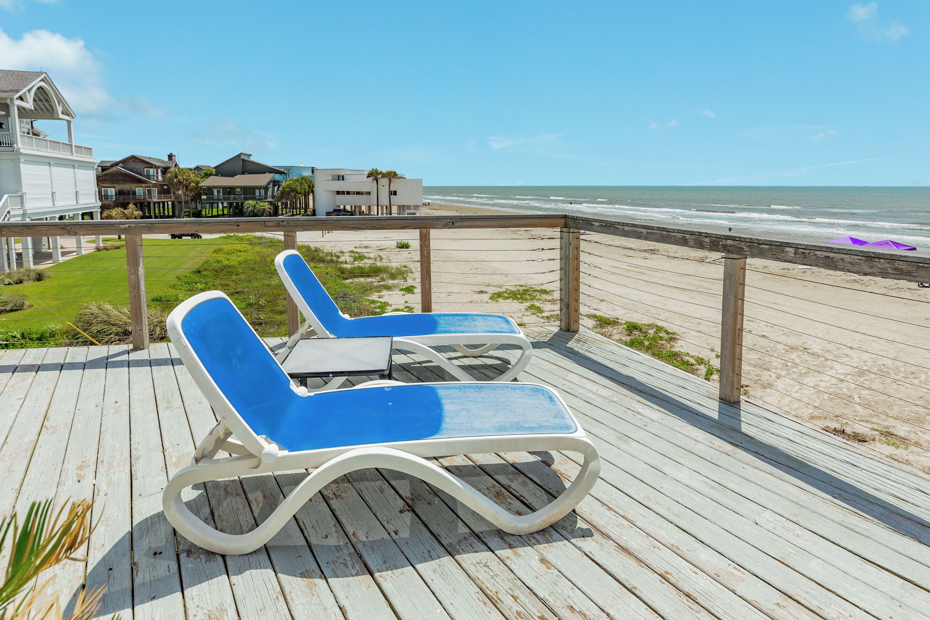 Eine Holzterrasse mit zwei Liegestühlen, die zum Meer ausgerichtet sind.