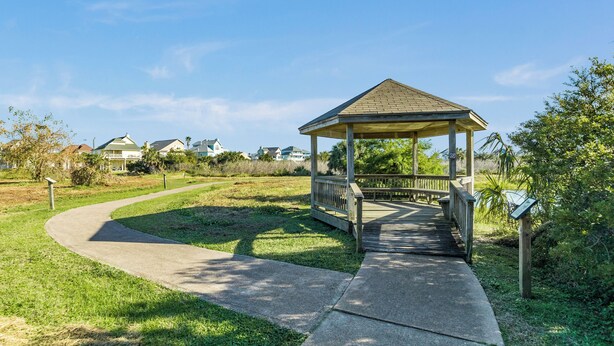 Um gazebo com deck de madeira, cercado por gramado e um caminho curvo.