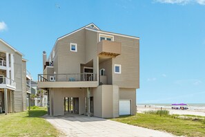 A multi-story residential building with a balcony, a garage, and a view of the beach. - Steps from the Beach, Pet Friendly, Warm Interior with Great Views (Galveston)