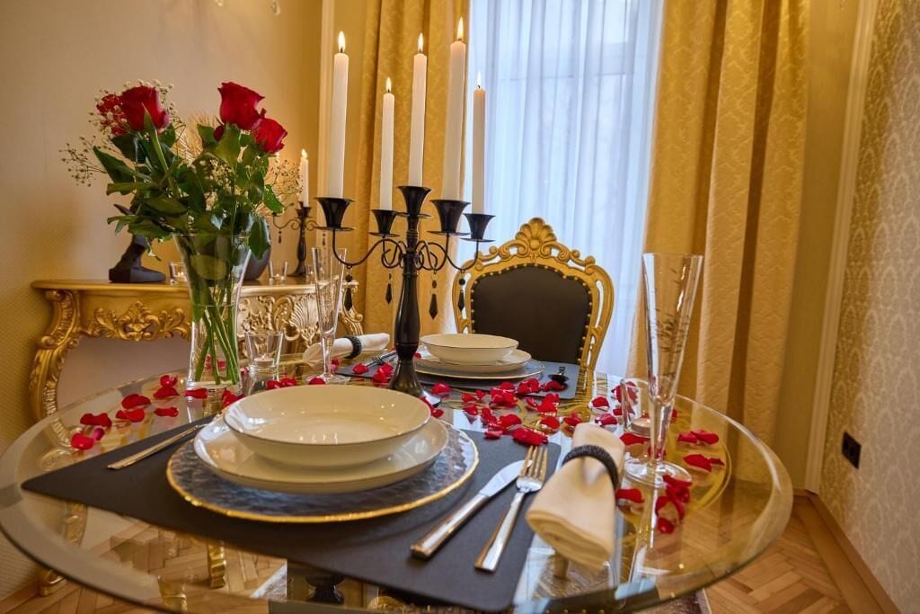 Mesa de comedor formal con platos blancos, cubiertos negros y un jarrón con rosas rojas.
