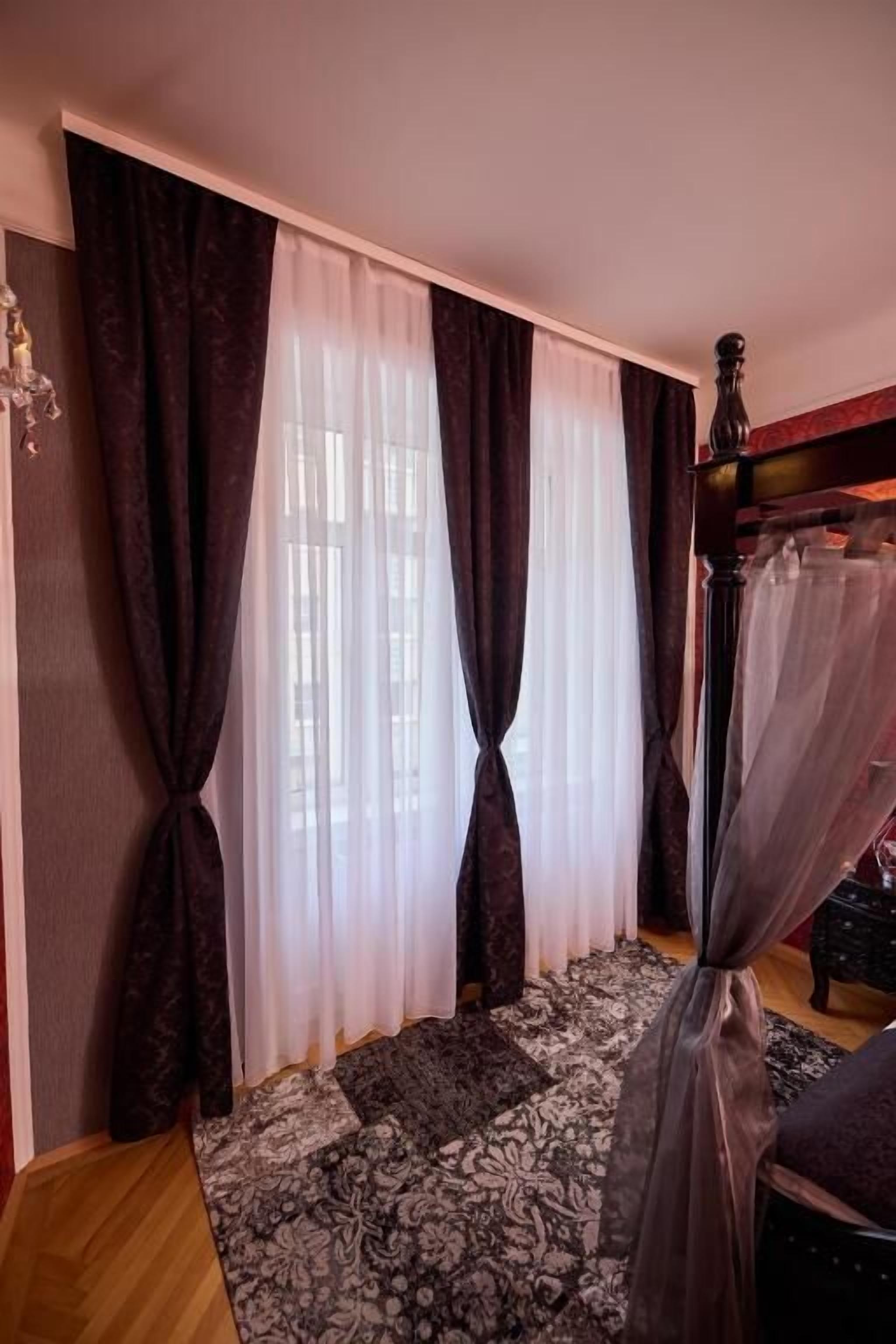Un dormitorio con cama, ventana con cortinas y mesita de noche.