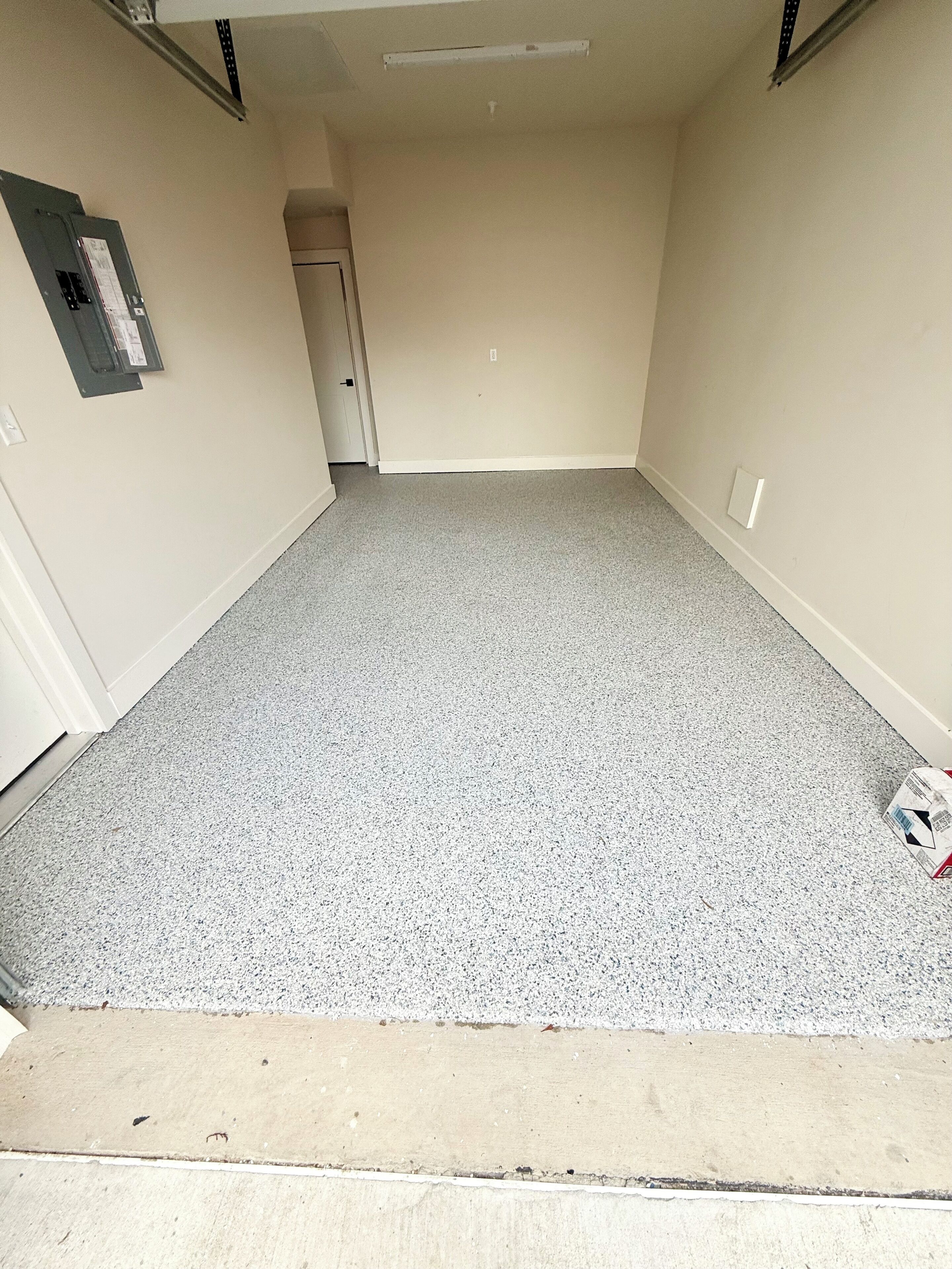 Une pièce avec un sol gris à motifs, une porte et un interrupteur sur le mur.