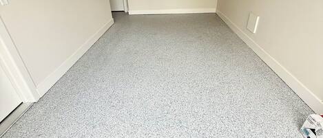 A room with a grey speckled floor, a door, and a light switch on the wall.