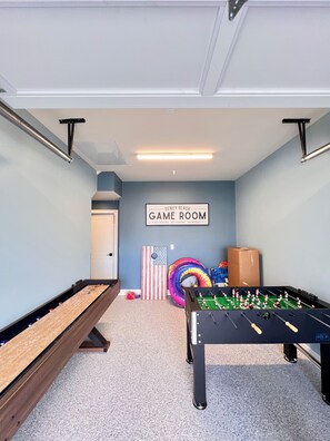 Een speelkamer met een tafelvoetbaltafel, biljarttafel en een bord waarop staat 'DEWEY BEACH GAME ROOM'.