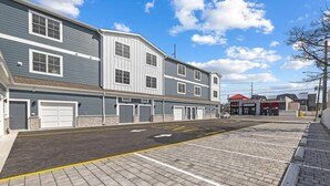 A parking lot with multiple garage doors, a clear sky, and a building with a red roof in the background. - New Spacious 5-bedroom condo in the heart of fabulous Dewey Beach (Dewey Beach)