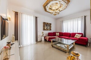 Un salón amplio con un sofá rojo, una mesa de centro de vidrio y una araña.