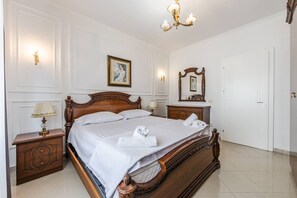 A neatly made bed with a wooden headboard, a bedside table with a lamp, and a wall-mounted mirror. - Historic Quarter Stay | 1BR Apartment by PikHost (Shkodër)