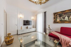 Una sala de estar moderna con una mesa de centro de vidrio, un sofá rojo, un televisor y un cuadro clásico en la pared.