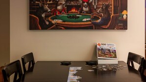A room with a large painting of deer at a poker table, a puzzle box, and a lamp on a table. - Right Mtn Attitude · Arcade, Hot Tub & Fire Pit (Berkeley Springs)