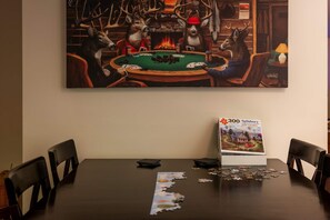 A room with a large painting of deer at a poker table, a puzzle box, and a lamp on a table. - Right Mtn Attitude · Arcade, Hot Tub & Fire Pit (Berkeley Springs)