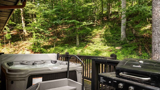 A hot tub and grill on a deck with a forest backdrop. - Right Mtn Attitude · Arcade, Hot Tub & Fire Pit (Berkeley Springs)