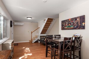 A dining area with a wooden table and chairs, a staircase, and a painting on the wall. - Mountain Cabin with Arcade, Hot Tub & Fire Pit (Berkeley Springs)