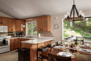 Une cuisine moderne avec des meubles en bois, un îlot central et un coin repas offrant une vue sur l’extérieur.