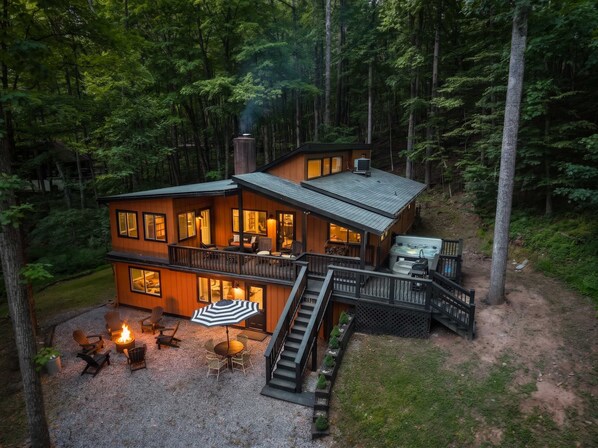 Eine zweistöckige Holzhütte mit einer Terrasse, Sitzgelegenheiten im Freien und einem Whirlpool.