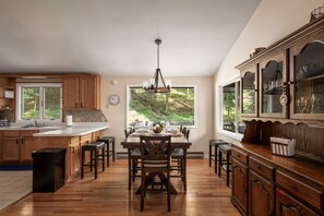 A spacious kitchen with wooden cabinets, a dining area with a large window, and a view of greenery outside. - Right Mtn Attitude · Arcade, Hot Tub & Fire Pit (Berkeley Springs)