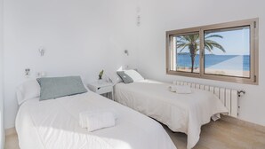 A hotel room with two beds, a window with a beach view, and a white color scheme. - Beachfront Villa With Pool, Puerto Pollenca (Pollença)