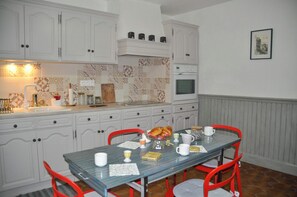 Eine Küche mit weißen Schränken, einer gefliesten Spritzschutzwand, einem eingebauten Backofen und einem Esstisch mit Stühlen.