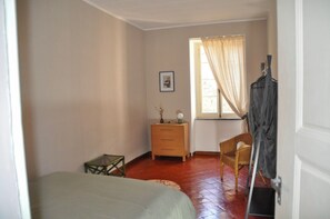 Ein Zimmer mit einem Bett, einem kleinen Tisch, einem Stuhl, einem Schminktisch und einem Fenster mit Vorhängen.