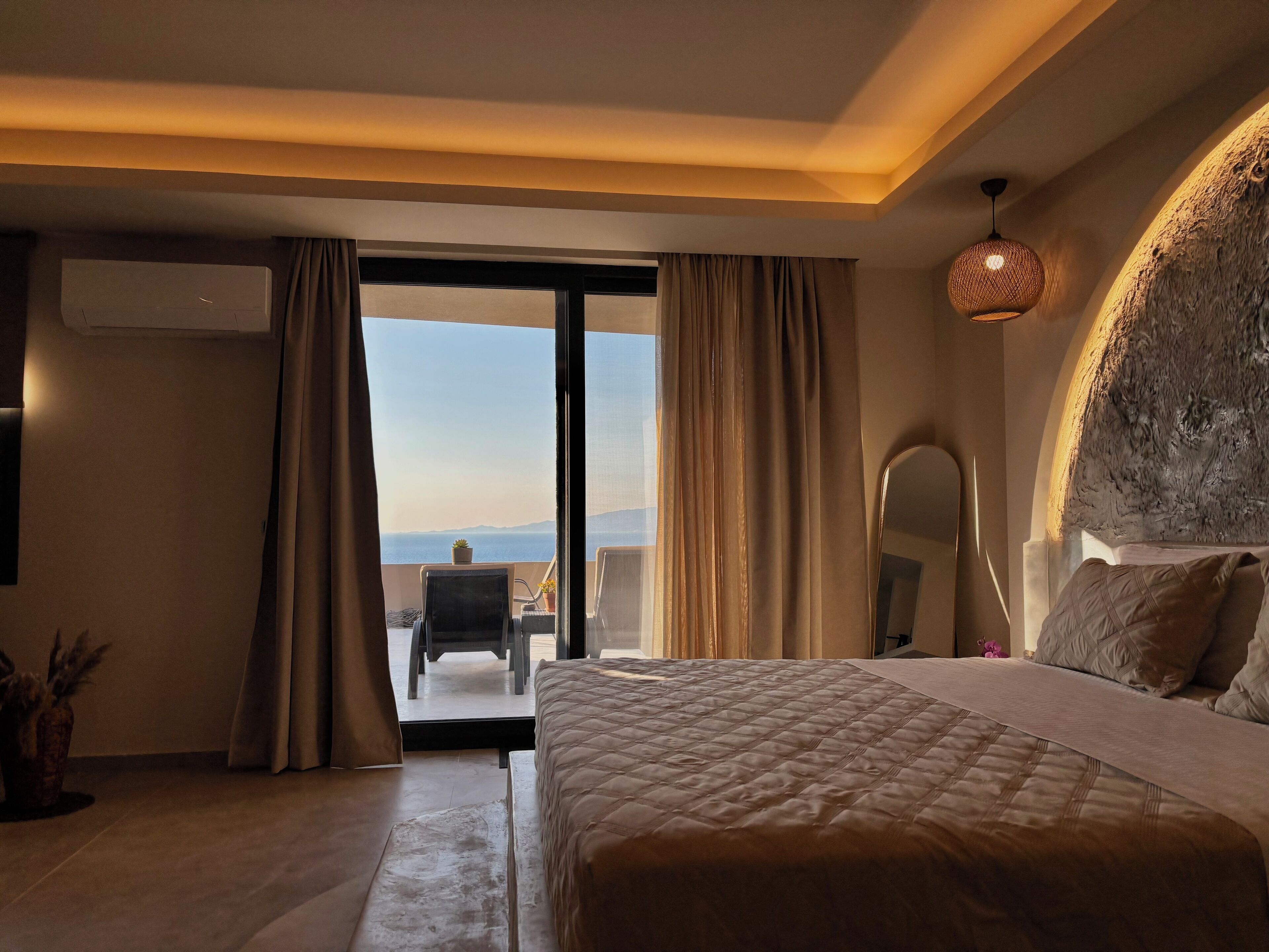 Quarto de hotel com uma cama grande, varanda com uma cadeira e vista para o mar.