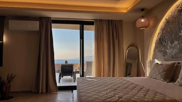 Quarto de hotel com uma cama grande, varanda com uma cadeira e vista para o mar.