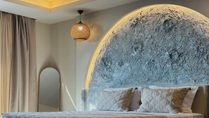 A bedroom with a large bed, a headboard with a textured design, a hanging light fixture, and a mirror. - Bevimar Moonlight Suite with Private Pool and Non Heated Jacuzzi (Finikia)
