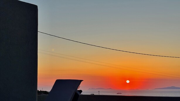 A sunset view from a balcony with a chair, a power line, and a distant ship. - Bevimar Moonlight Suite with Private Pool and Non Heated Jacuzzi (Finikia)
