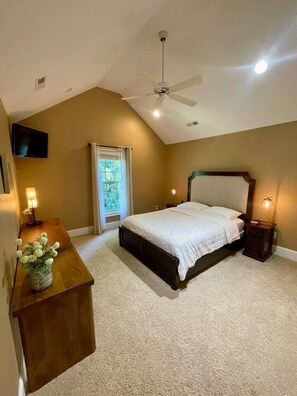 Ein Schlafzimmer mit einem Bett, einem Deckenventilator, einem an der Wand montierten Fernseher und einem Fenster mit Vorhängen.