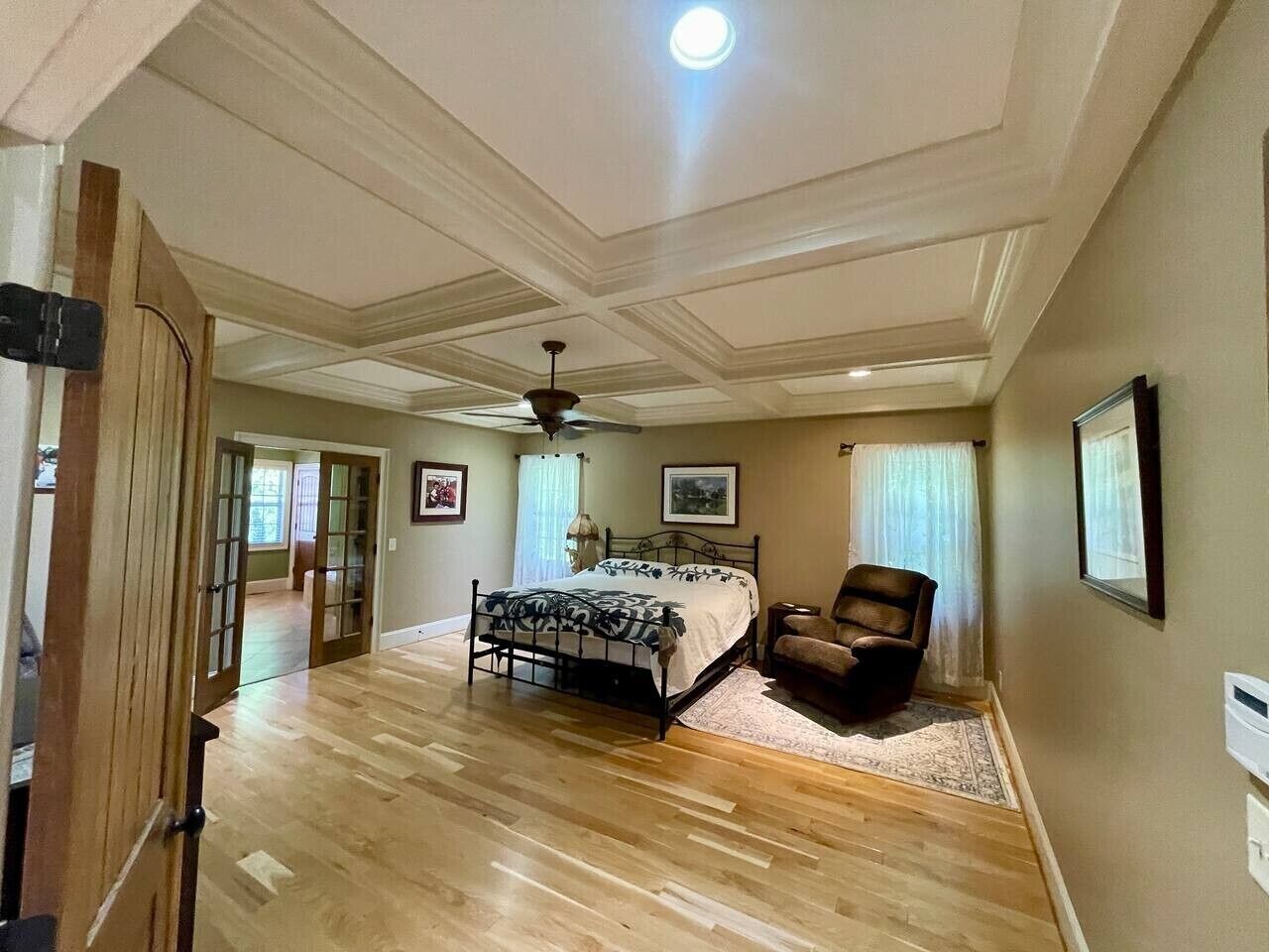 Un dormitorio con cama, una silla, ventilador de techo y una puerta que da a otra habitación.