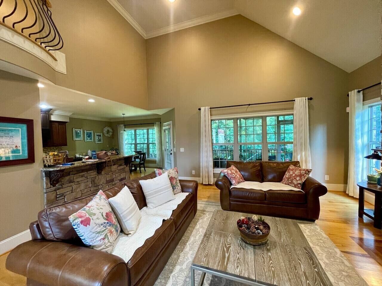 A spacious living room with a stone fireplace, leather sofas, a coffee table, and large windows offering a view of the outdoors.