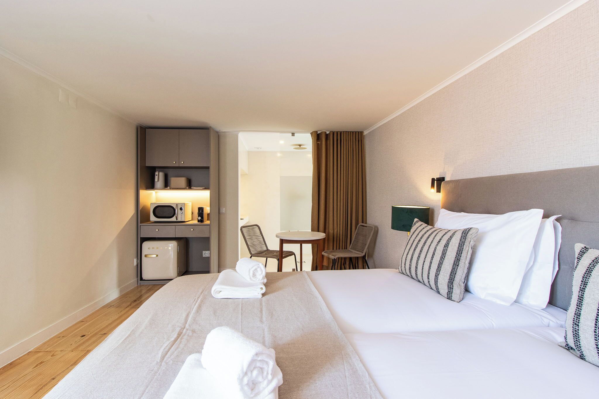 Habitació d'hotel amb llit, escriptori, cadira, barra minibar i vista al passadís.