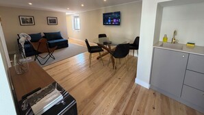 Ein modernes Wohnzimmer mit einer Couch, einem Esstisch mit Stühlen, einer Küchenzeile mit Spüle und Schränken sowie einem flachbildfernseher an der Wand.