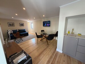 A modern living room with a sofa, a dining table with chairs, a kitchen area with a sink and cabinets, and a flat-screen TV mounted on the wall. - St. Michael Studios  (Lisboa)
