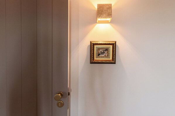 A closed door with a brass handle and a keyhole, a wall-mounted light fixture, and a framed picture. - St. Michael Studios (Lisboa)