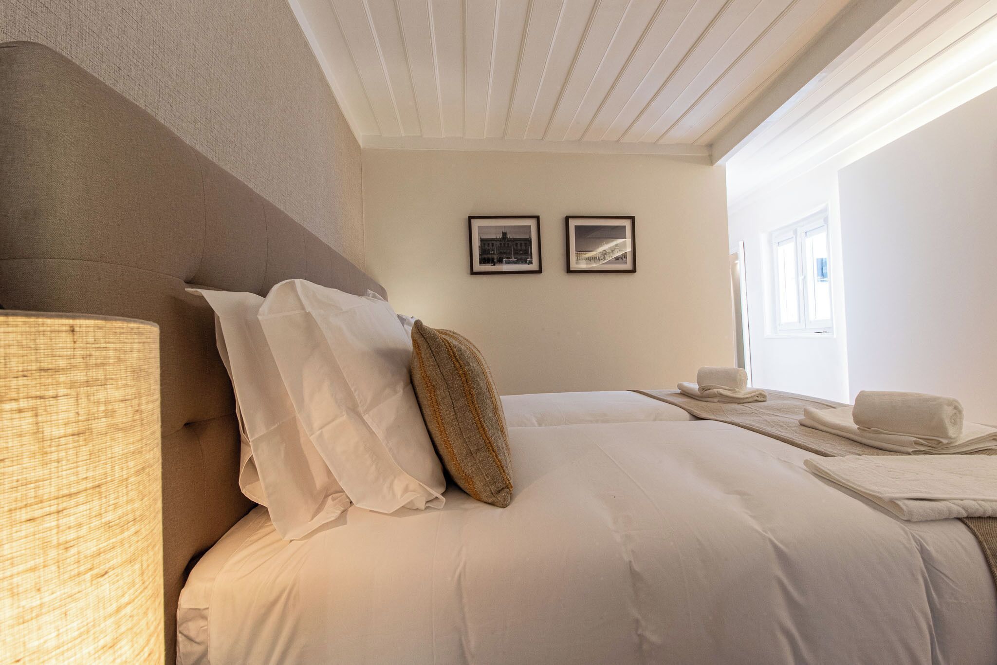 Una cama bien hecha con ropa blanca, un cabecero y dos cuadros en la pared.