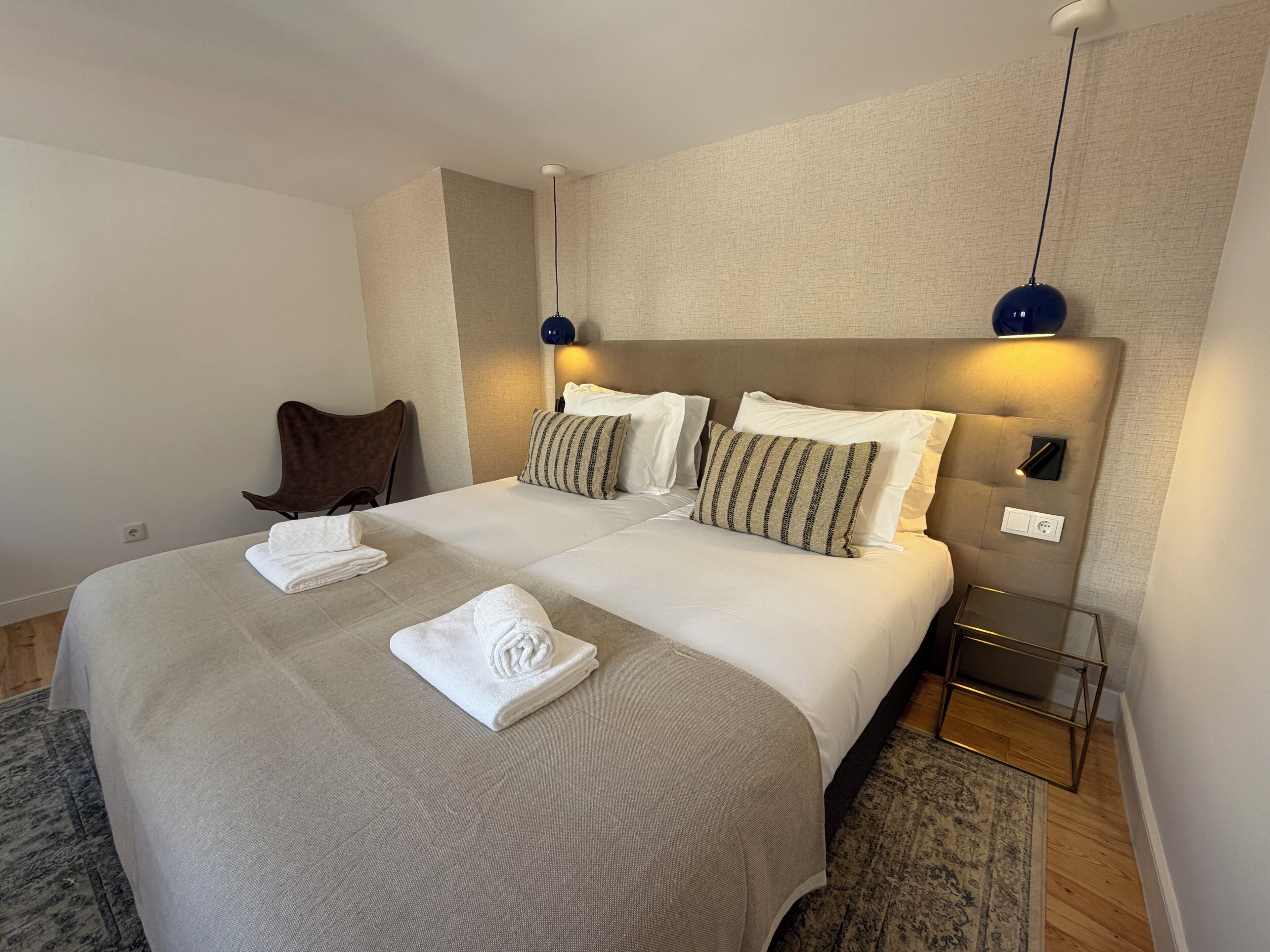Een hotelkamer met een groot bed, twee nachtkastjes, een stoel en een bijzettafeltje.