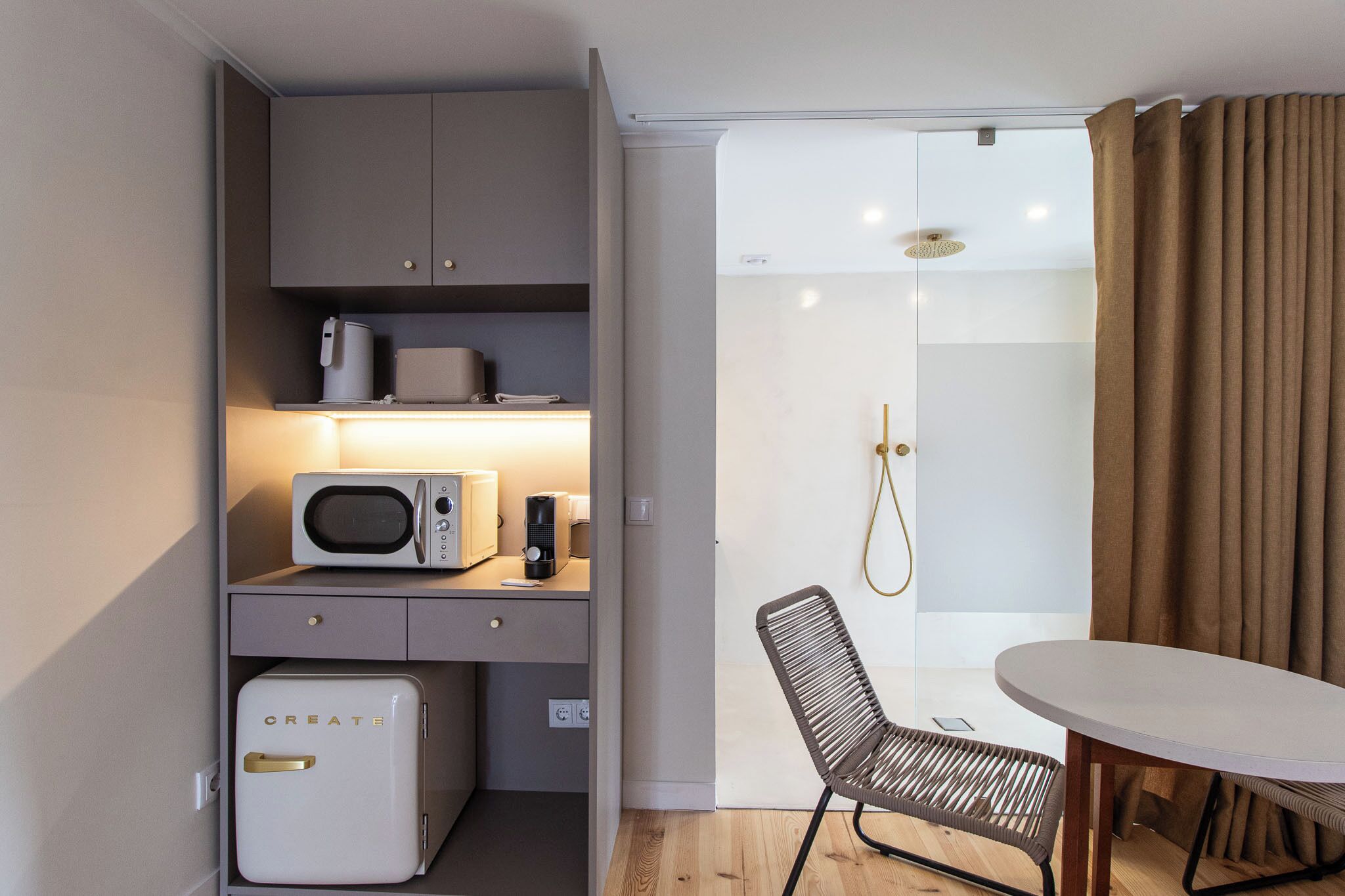 Ein kleines Hotelzimmer mit Küchenzeile, Duschbereich und Esstisch.
