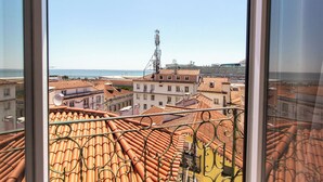 Blick aus einem Fenster auf orangefarbene Ziegeldächer und ein entferntes Gewässer.