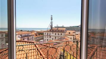 A view from a window overlooking terracotta-tiled rooftops and a distant body of water.