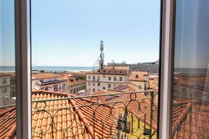 A view from a window overlooking terracotta-tiled rooftops and a distant body of water. - St. Michael Studios  (Lisboa)
