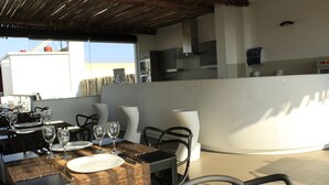 Un espacio exterior para comer con mesas dispuestas para dos personas, equipado con platos, cubiertos y copas de vino.