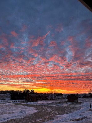Un paisaje rural con cielo al atardecer, suelo cubierto de nieve y un edificio pequeño.