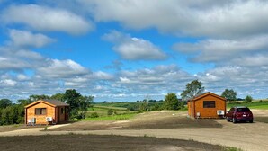 Twee houten blokhutten met aanhangende garages, omgeven door open velden en een heldere lucht.