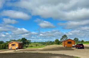 Dos cabañas de madera con garajes anexos, rodeadas de campos abiertos y un cielo despejado.