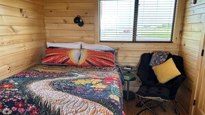 Een houten kamer met een bed, een stoel, een klein tafeltje en een raam met jaloezieën.