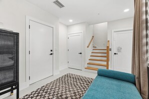 A hotel room with a checkered rug, a bed with a teal cover, a black chair, and a staircase leading to another room. - Rooftop Hot Tub, City Views, Walk to Downtown (Sarasota)