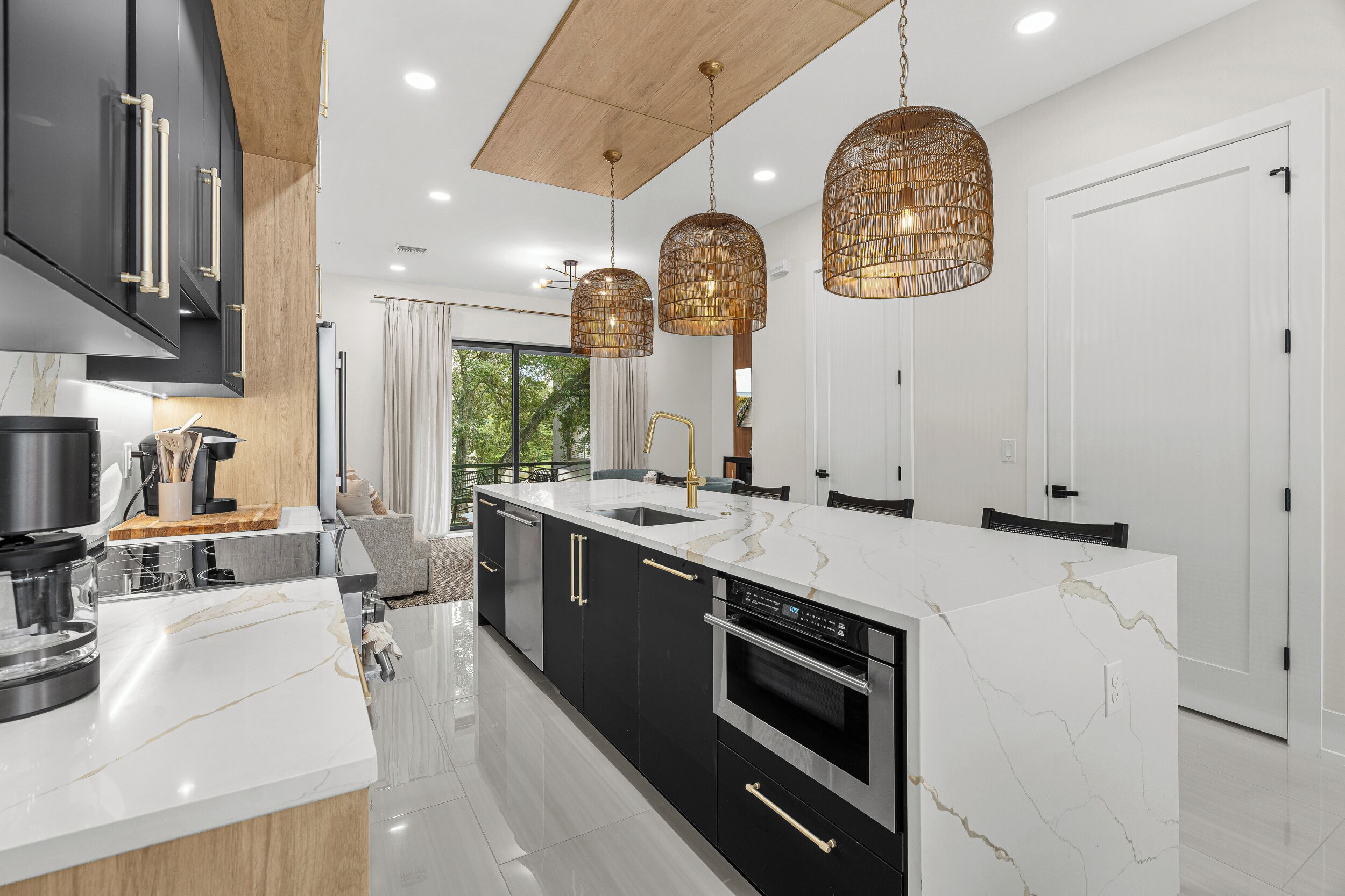 A modern kitchen with a central island, black cabinets, stainless steel appliances, and pendant lighting.
