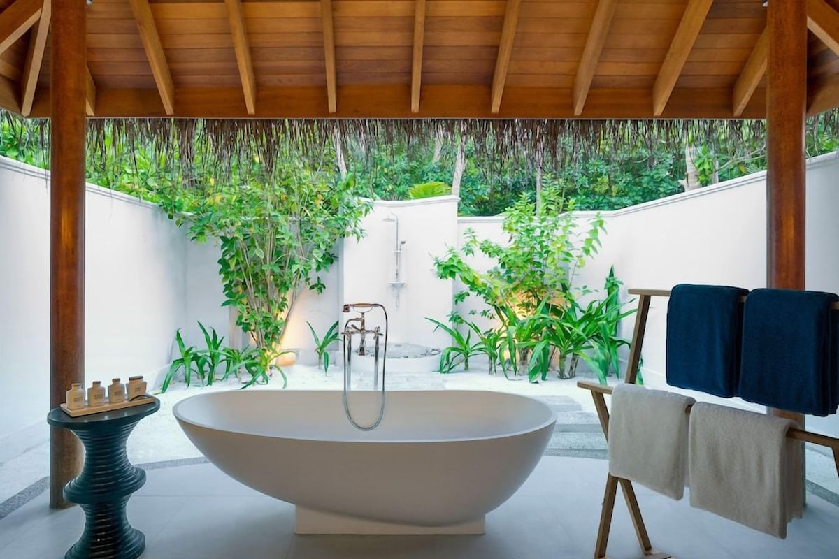 A modern bathroom with a freestanding bathtub, a small table with bottles, and a towel rack.