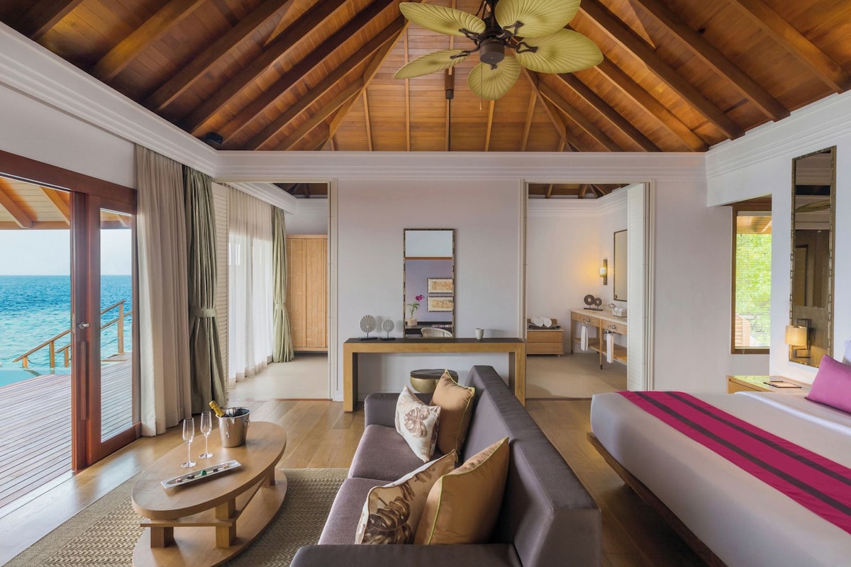 A spacious living area with a wooden ceiling, a sofa, a coffee table, and a view of the ocean.
