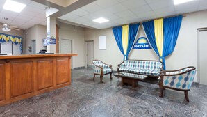 A reception area with a wooden desk, two upholstered chairs, a sofa, and a sign for complimentary breakfast. - Days Inn by Wyndham Orangeburg (Orangeburg)